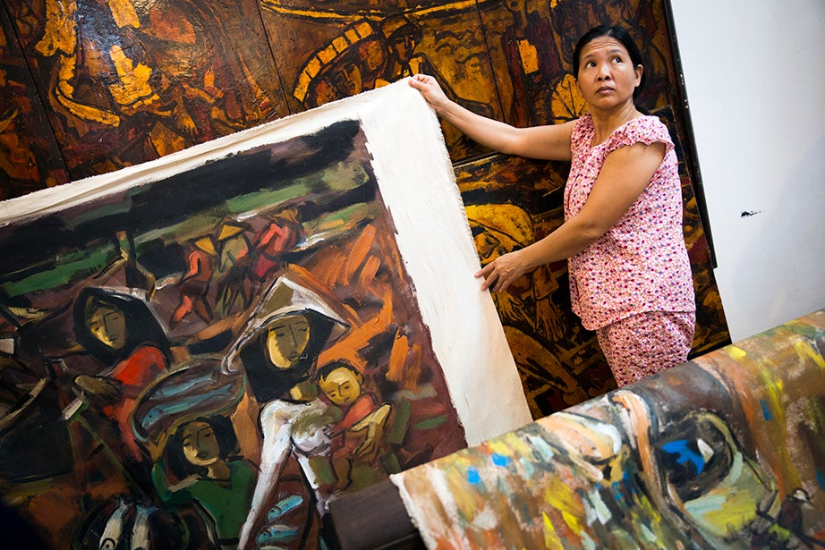 In the Hanoi studio of veteran and artist Pham Luc in Hanoi, Dao Thi Lien (pictured) arranges his works for display during Drew Faust’s visit.