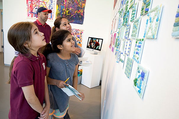 Gardner Pilot Academy third-graders Sophia Deoliveira (left) and Mariaeliza Vasquez and Vasquez's parents look for the girls' artwork on display at the Harvard Ed Portal.