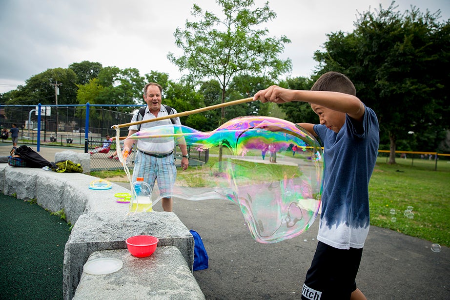 Jeffrey Peilco, 8, makes sure not to get wet while using a bubble kit that Kerry McGowan (left), Phillips Brooks House Association program director, made for the campers.