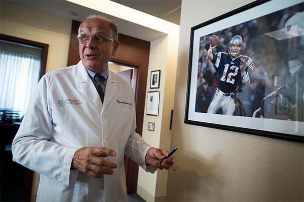 Orthopaedic Surgeon Bertram Zarins is pictured by a photograph of Tom Brady in his office at MGH.