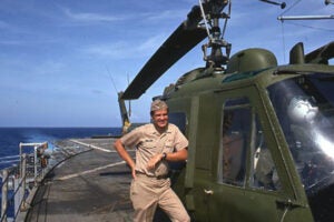Bertram Zarins poses in front of a helicopter on board the USS Okinawa.