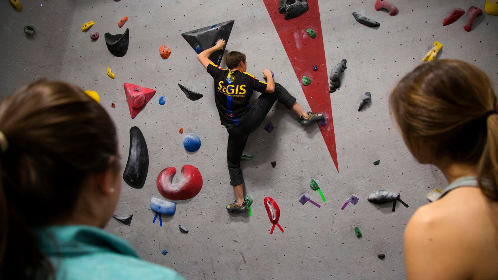 Kami Krista ’21 scales Harvard’s bouldering wall while members of the Climbing Club look on. 