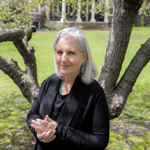 Terry Tempest Williams stands with hands clasped in front of a tree.