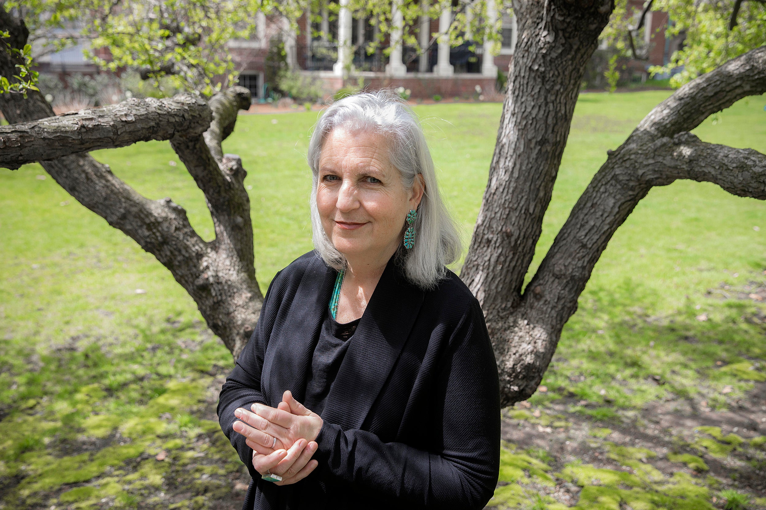 Terry Tempest Williams stands with hands clasped in front of a tree.