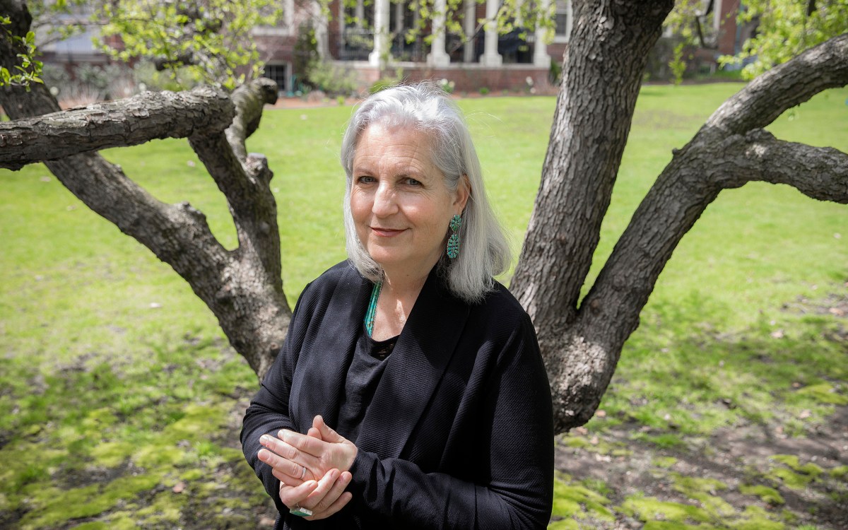 Terry Tempest Williams stands with hands clasped in front of a tree.