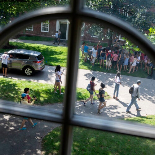 Students and their families mingle outside Mass Hall during move-in day. They are framed by a Harvard Hall window. 