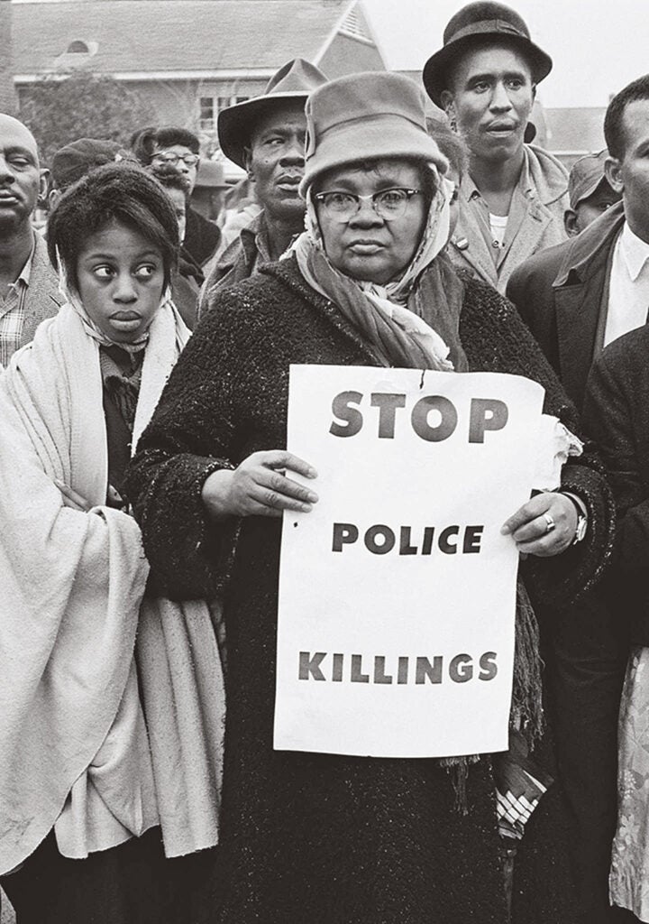 Women holds sign that says "Stop police killings" in 1965.