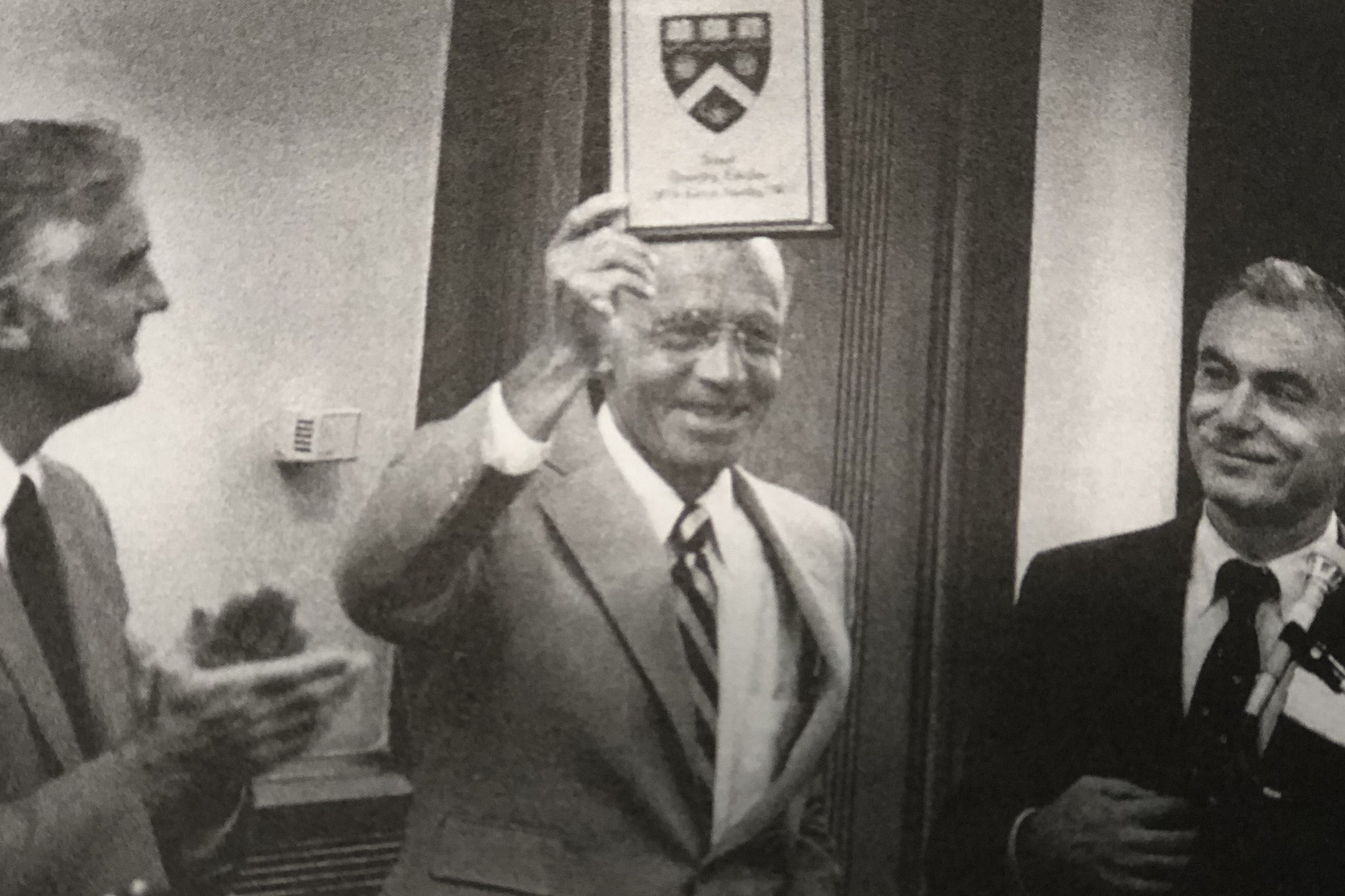 Three men in a black and white photo, the man in the middle is holding up an award