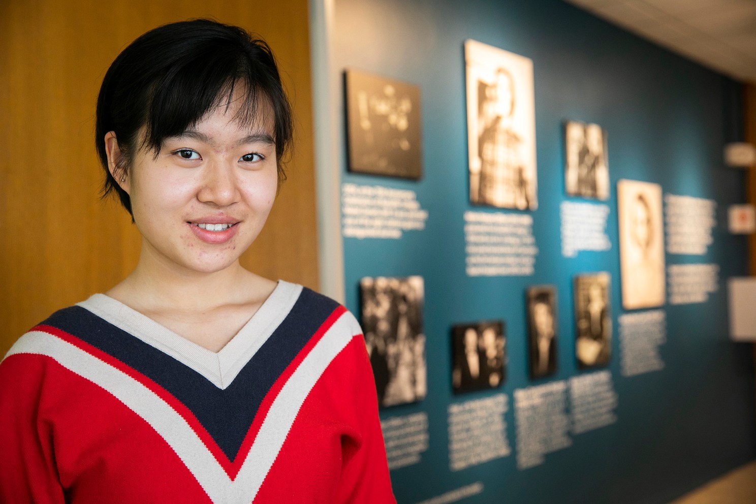 Xue (Snow) Dong in front of the photo wall in Currier House