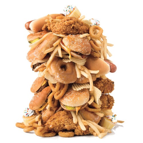 A tower of junk food including fried chicken, hamburgers, hot dogs, french fries, and cupcakes.