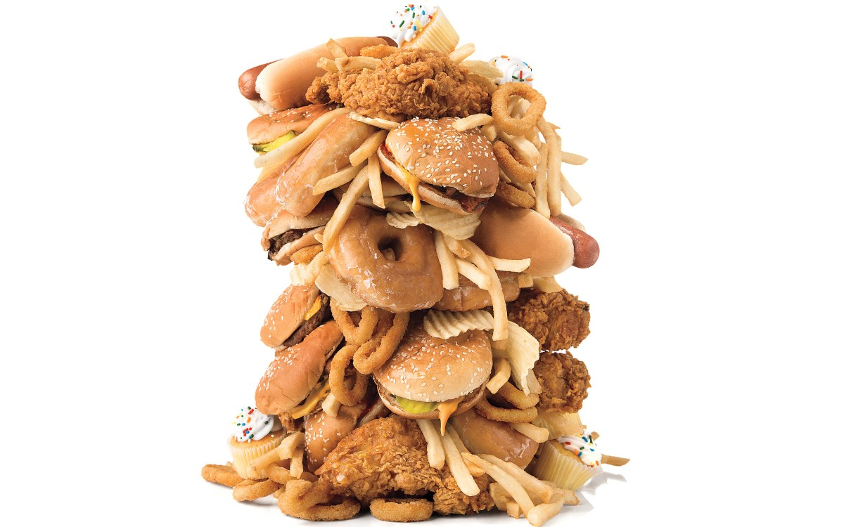 A tower of junk food including fried chicken, hamburgers, hot dogs, french fries, and cupcakes.