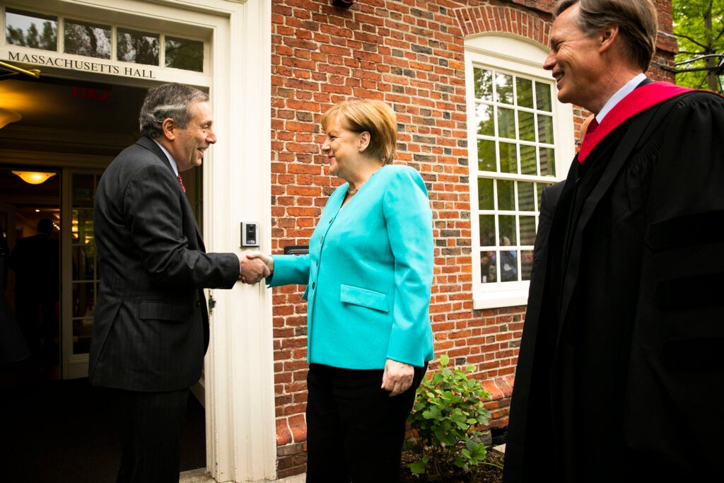 Larry Bacow shakes hands with Angela Merkel as Nick Burns looks on.