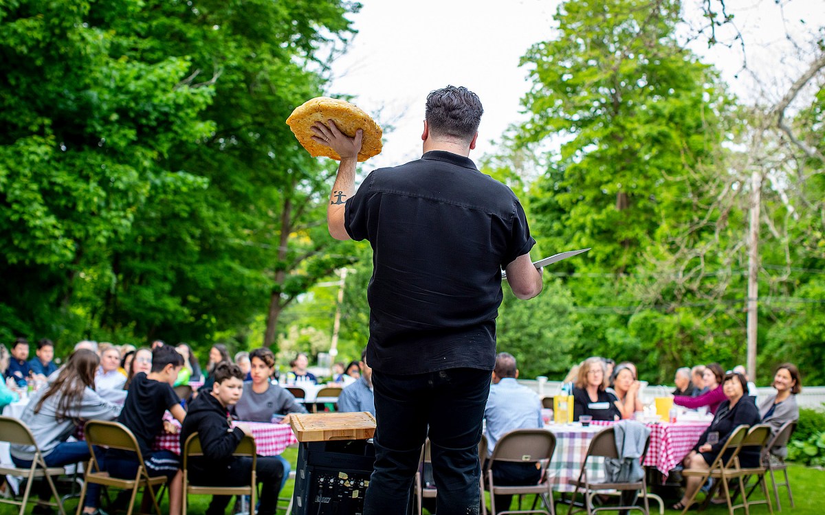 Israel Buffardi faces congregants sitting at tables outside, holding up focaccia he made for a Sacred Supper.