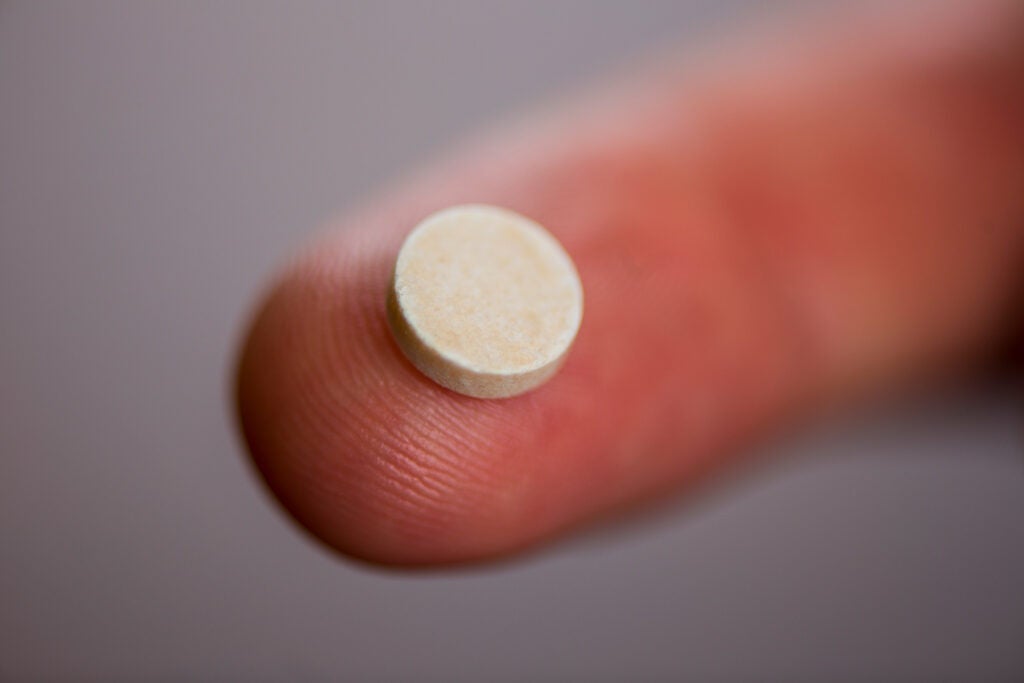A small white pill on a fingertip