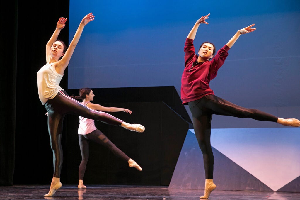 Dancers extend one leg in the air, arms outstretched.