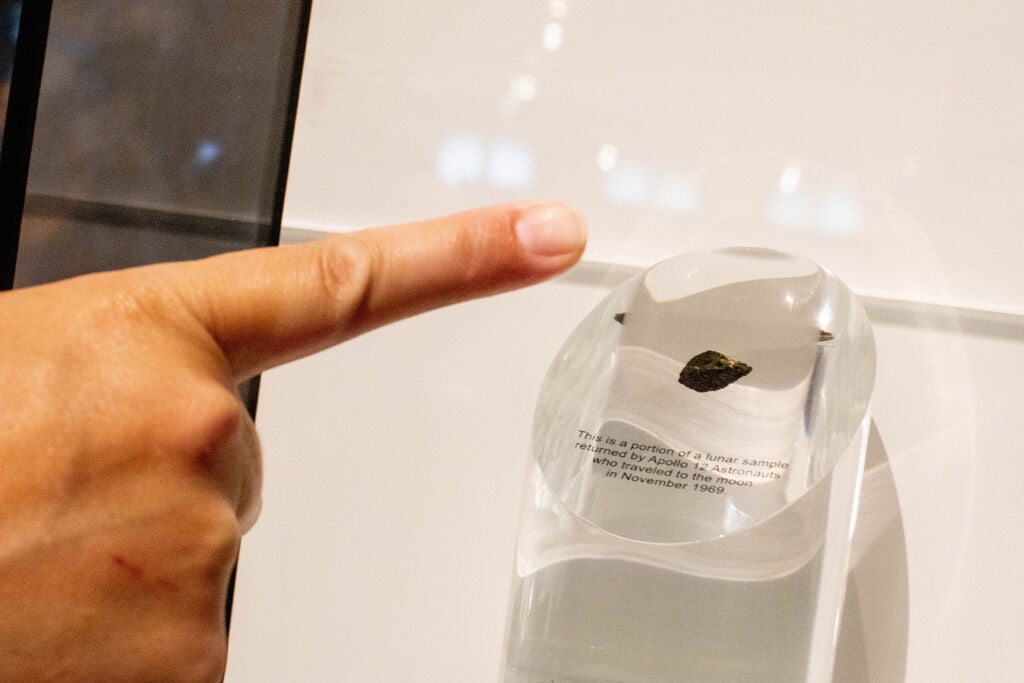 finger pointing at moon rock under glass
