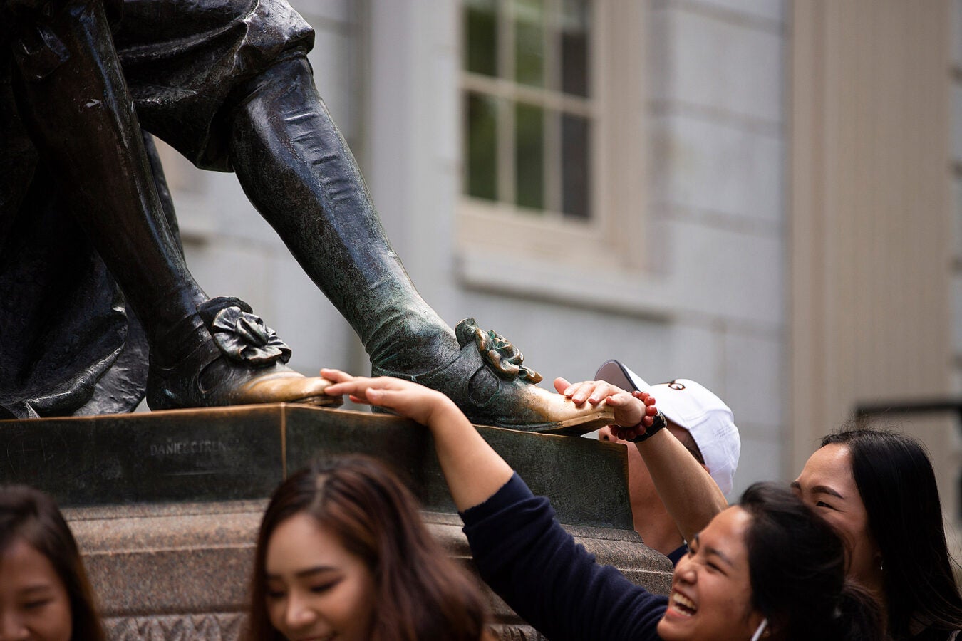 Tourists laugh, touch the feet of the statue.