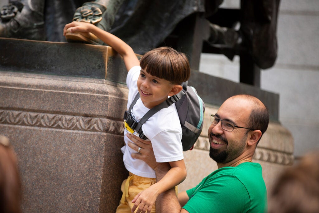 A father hoists his 7-year-old son to reach the foot of the statue.
