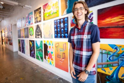 Harvard first year student standing in front of student artwork on wall.