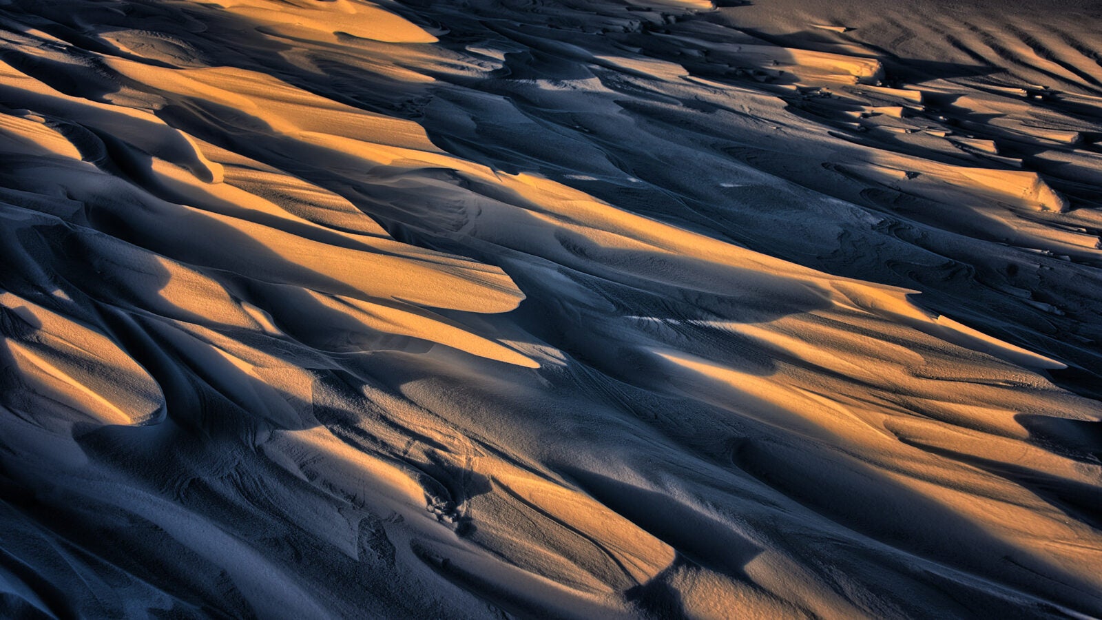 Dune-like formations sculpted by the wind called Sastrugi cast shadows on ice.