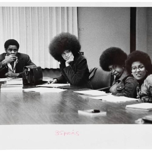 A black and white photo of young Angela Davis sitting at a conference table with three other people
