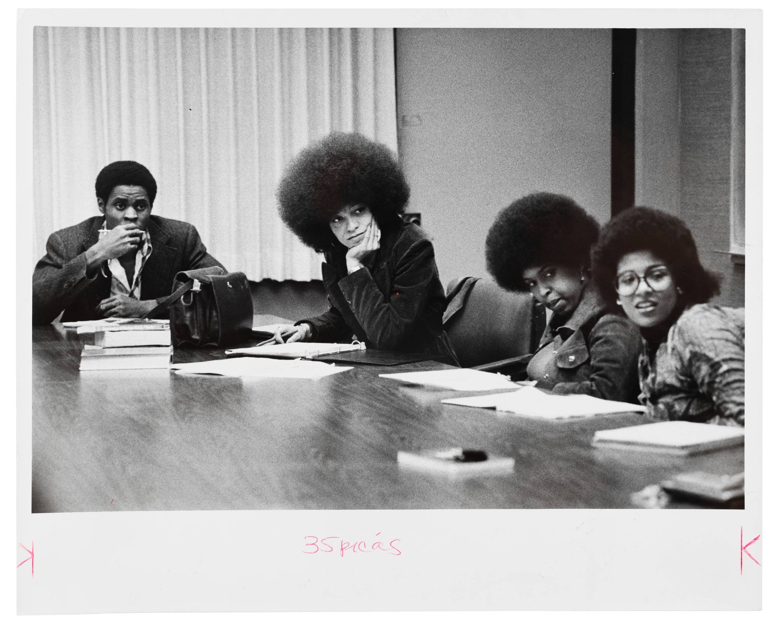 A black and white photo of young Angela Davis sitting at a conference table with three other people