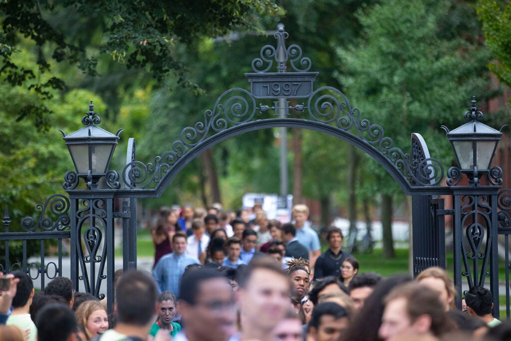 A large crowd of Harvard students walking through a Harvard gate.