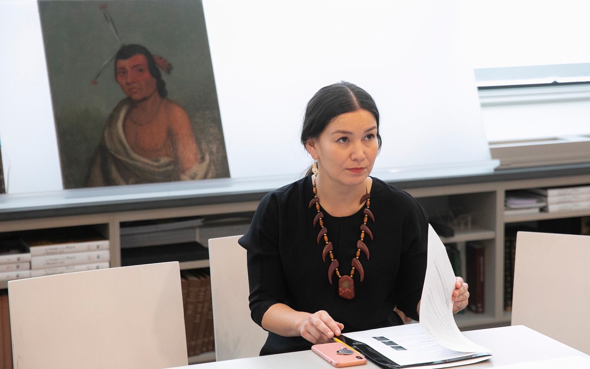 Professor looks up from papers on her desk; a portrait is behind her