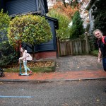 Polina Kehayova and Anna Kehayova ride scooters on the sidewalk, and Florian Engert rides rollerblades on the street.
