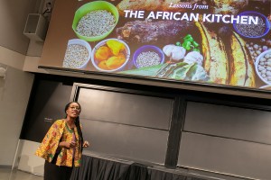 Selassie Atadika speaking in front of a projected image of African food