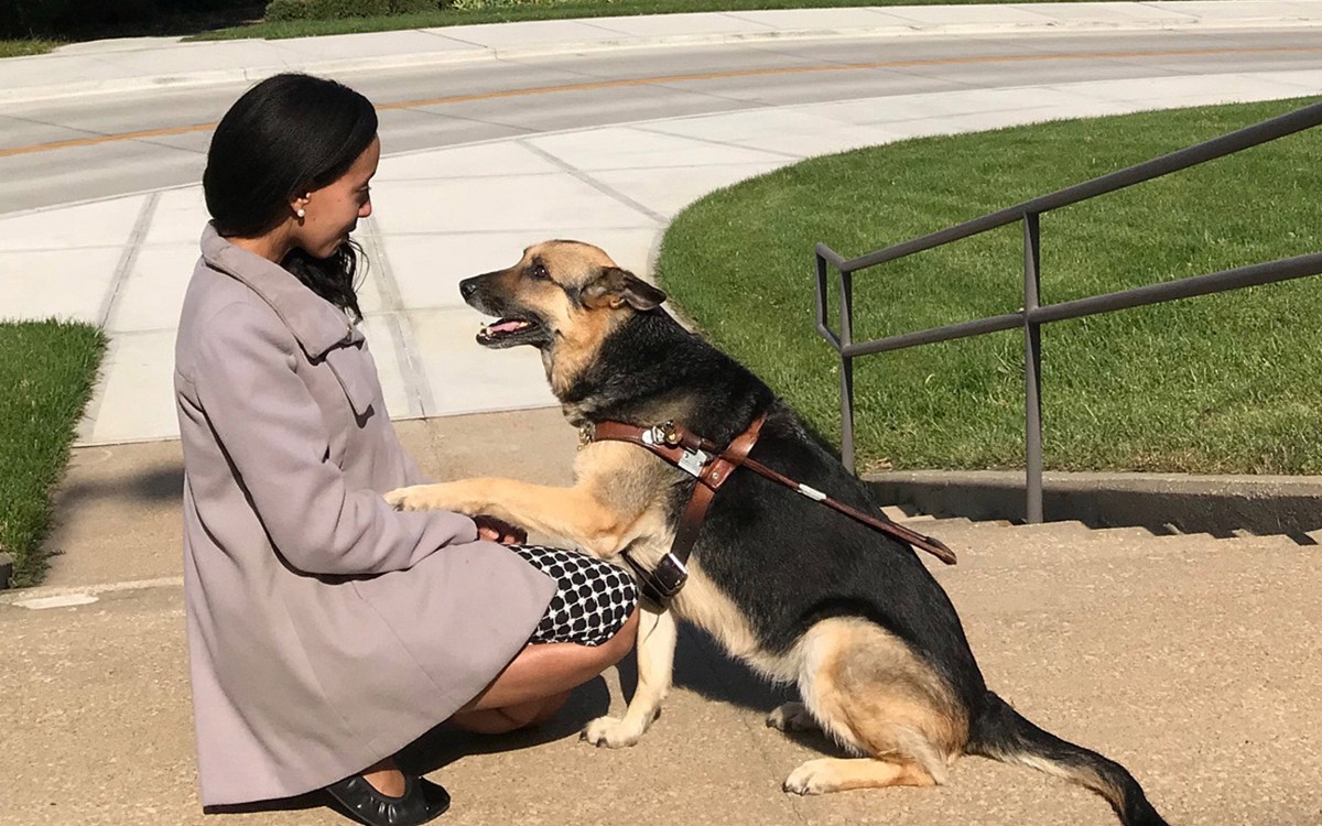 Haben Girma kneels with her dog, who has placed one paw on her knee