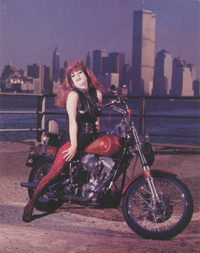 Joey Arias on motorcycle with New York City skyline in background.