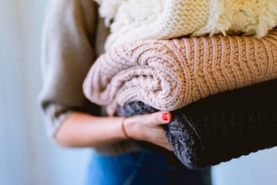 Close up of person's hands holding stack of folded sweaters.