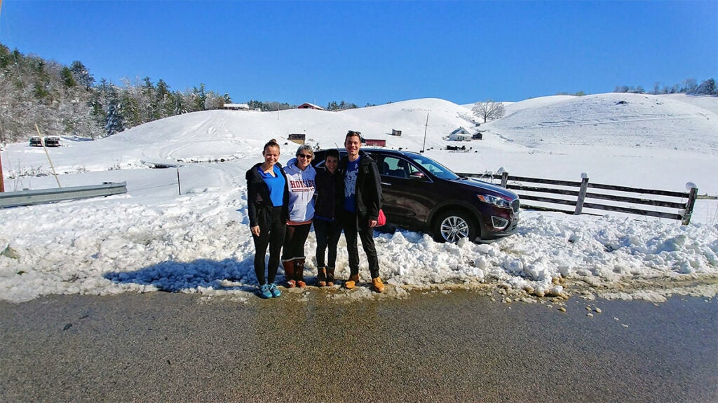 Andy Cohen and three women standing in front of their car stuck in the snow