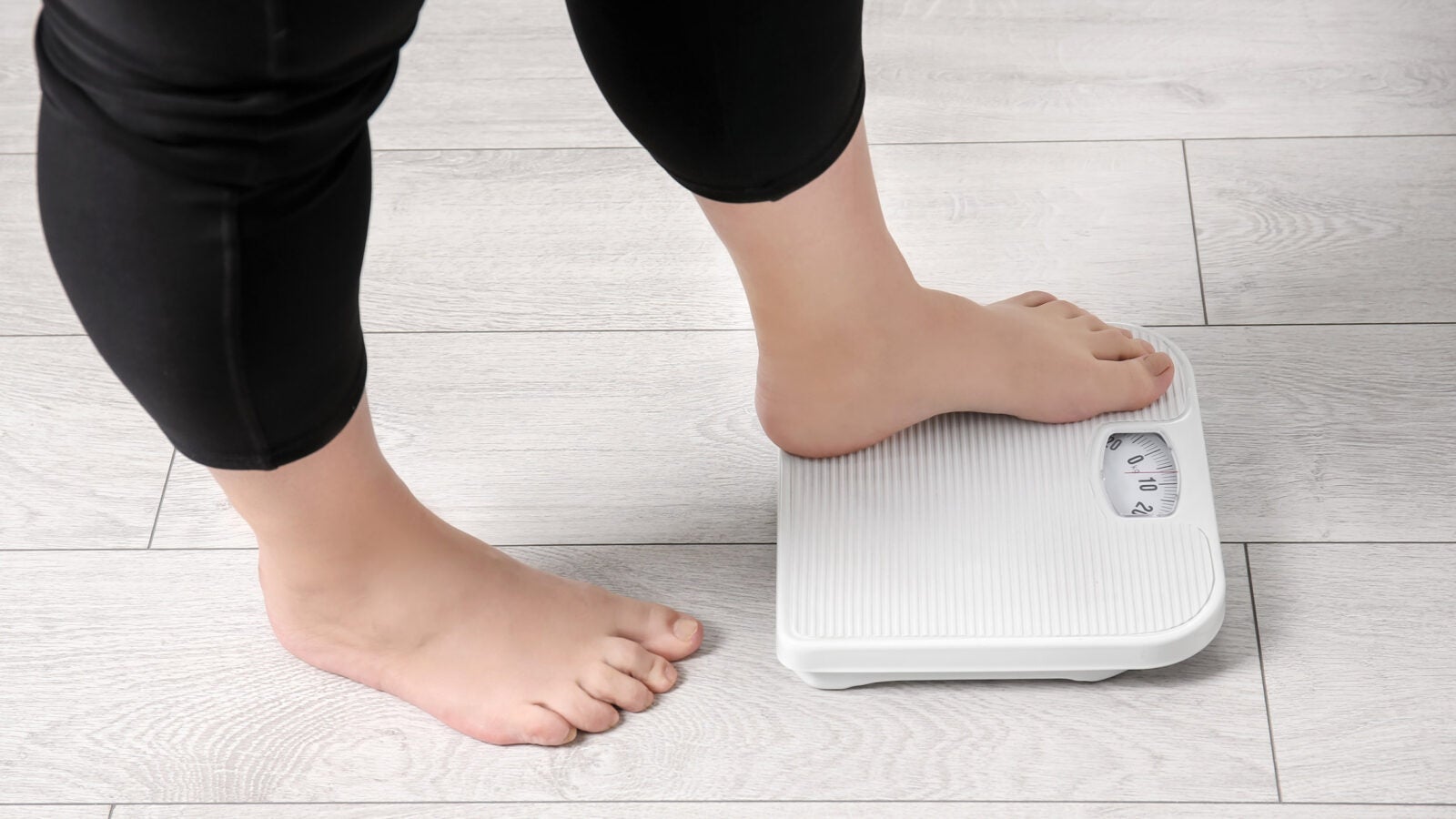 Overweight woman using scales indoors.