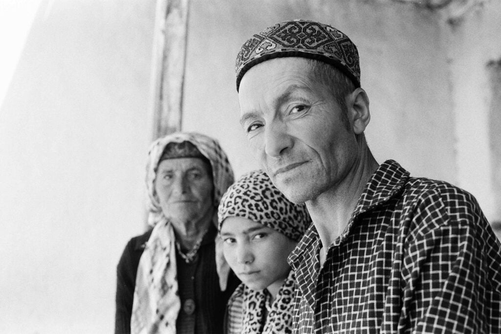 Qurbonsho, sitting beside his daughter and aunt, in front of his ancestral home.