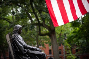 The John Harvard Statue is pictured with the American flat in Harvard Yard.