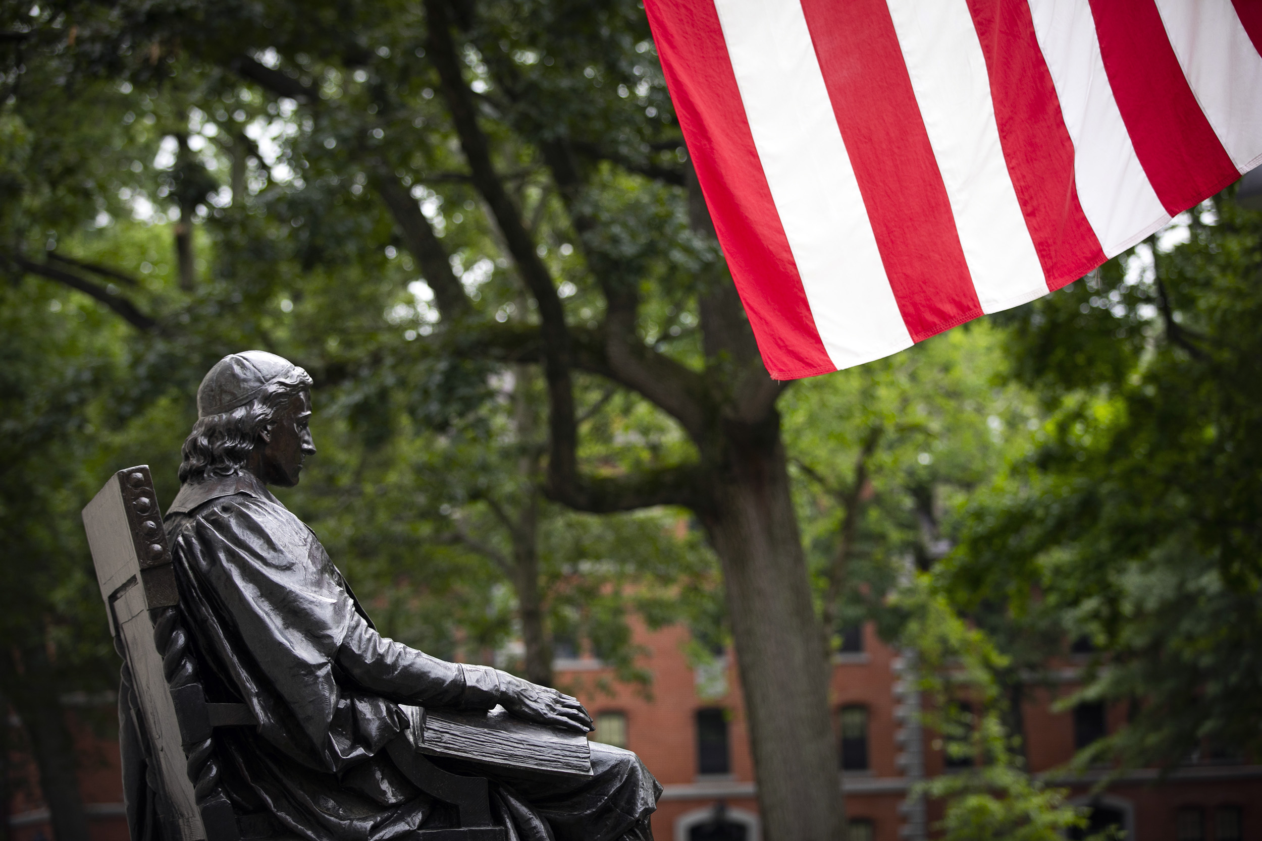 The John Harvard Statue is pictured with the American flat in Harvard Yard.