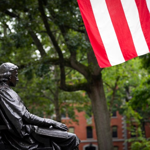 The John Harvard Statue is pictured with the American flat in Harvard Yard.