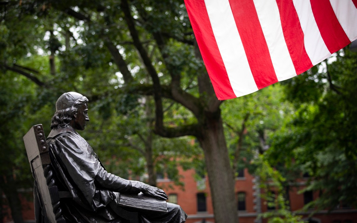 The John Harvard Statue is pictured with the American flat in Harvard Yard.