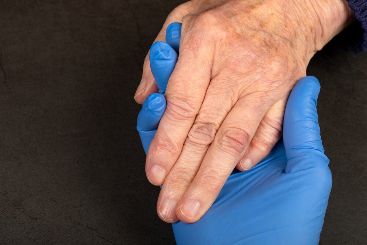 Caregiver holding elderly patients hand at home.