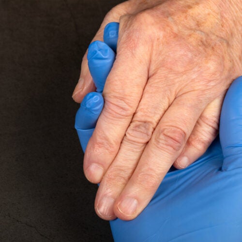 Caregiver holding elderly patients hand at home.