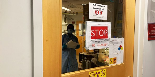 Researcher viewed through lab door posted with safety signs.