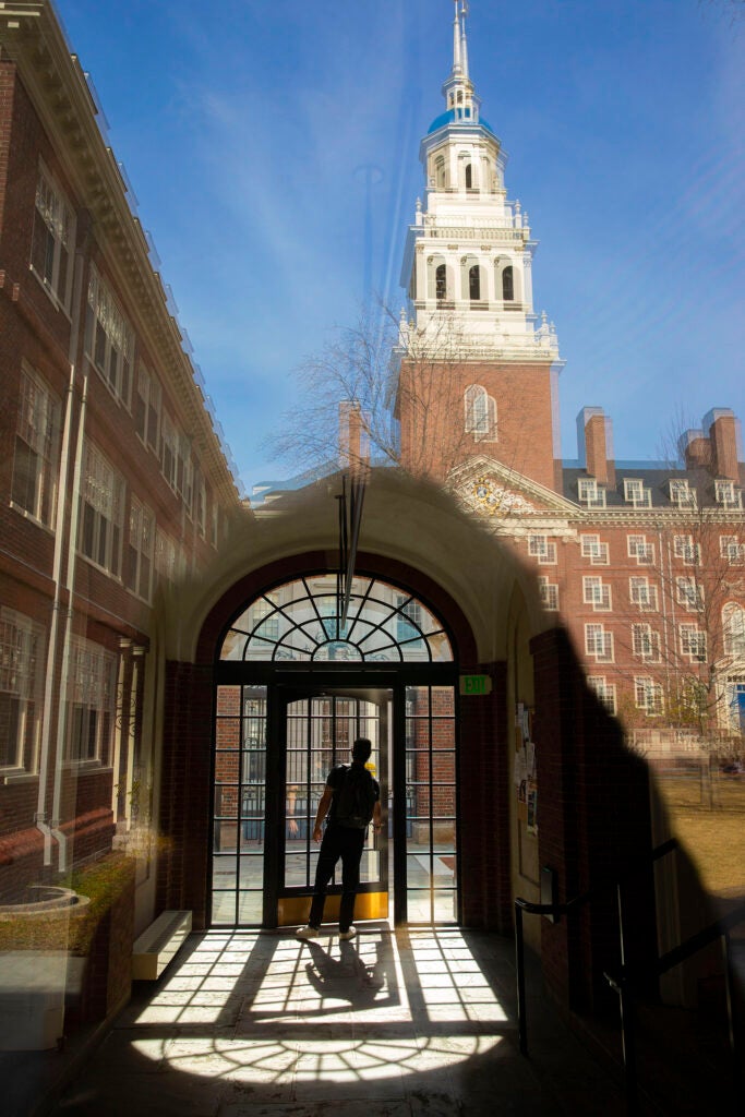 A student is framed by a bay window inside the passageway leading to the dining hall in Lowell House courtyard.