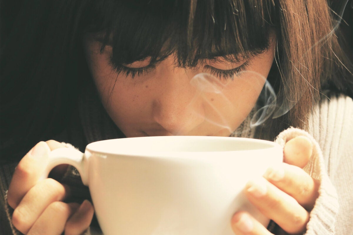 Person smelling a tasting a cup of tea.
