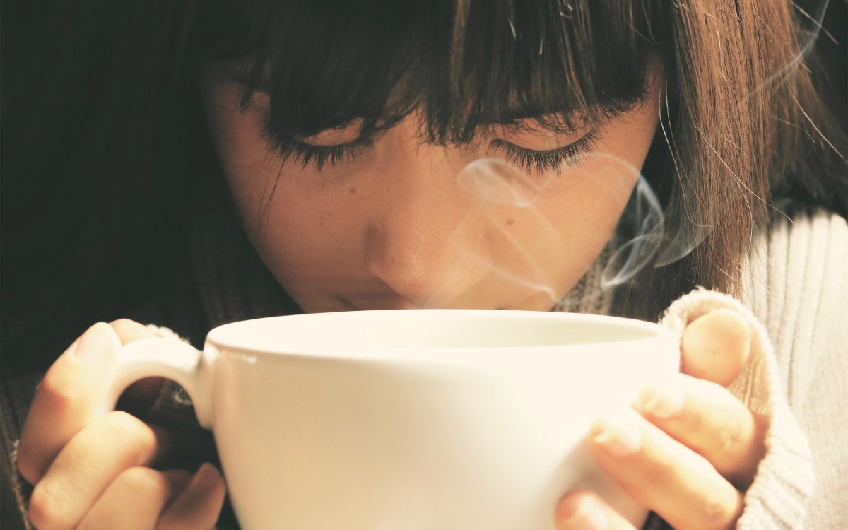 Person smelling a tasting a cup of tea.