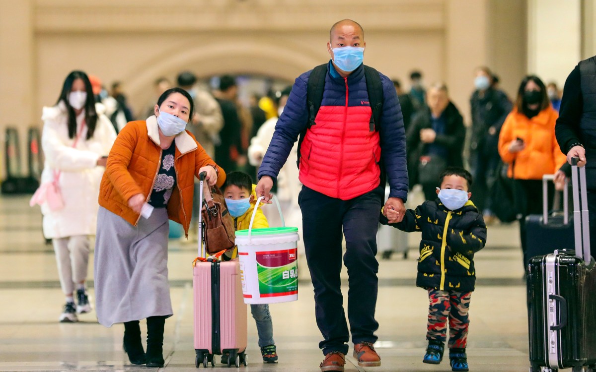 Masked travelers tote luggage in Wuhan in January.