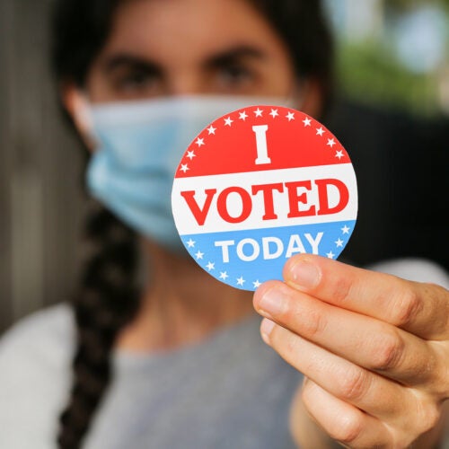 Young woman wearing face mask holding I voted today sticker.