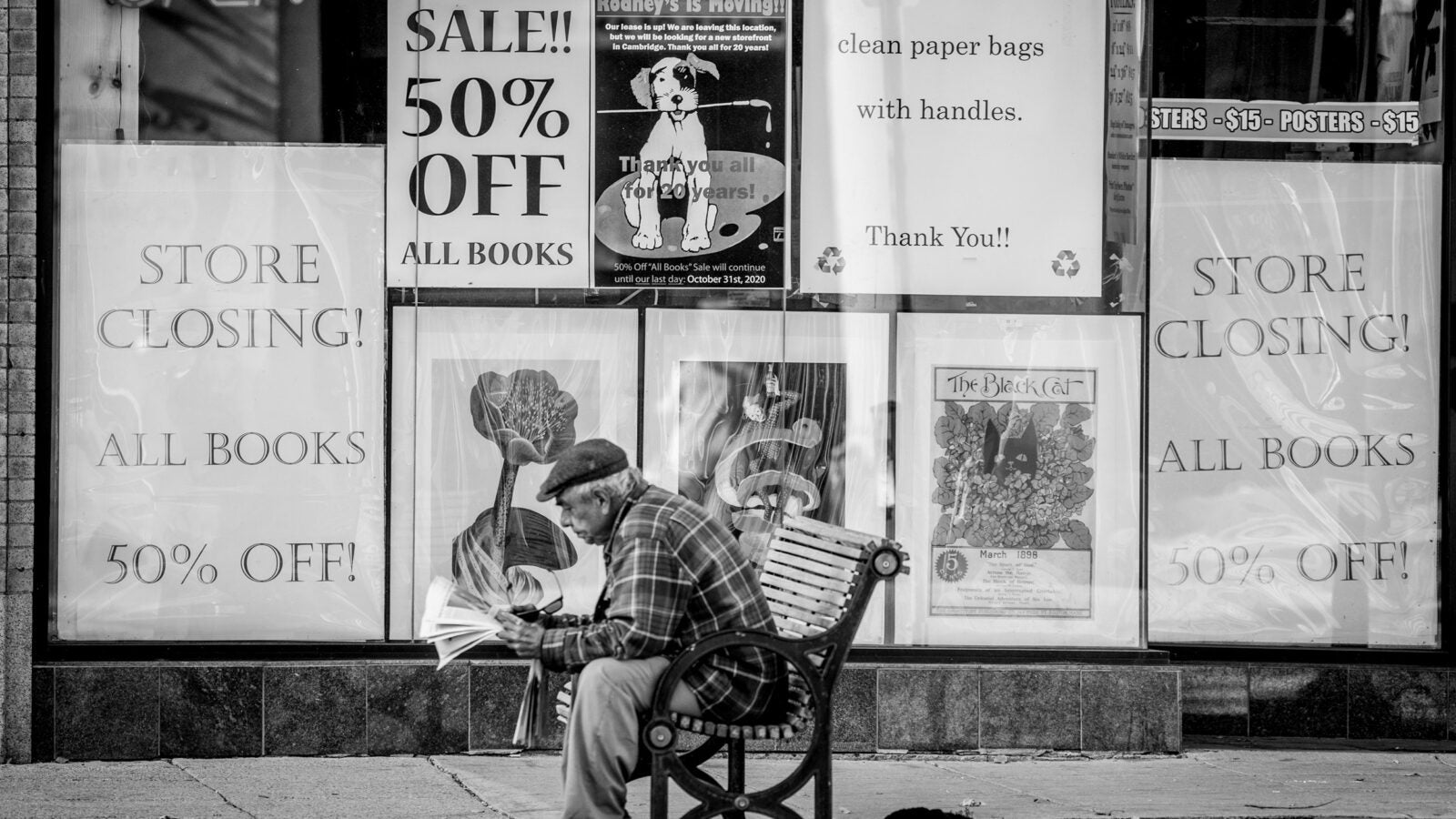 Man sitting on bench in front of store that is closing.