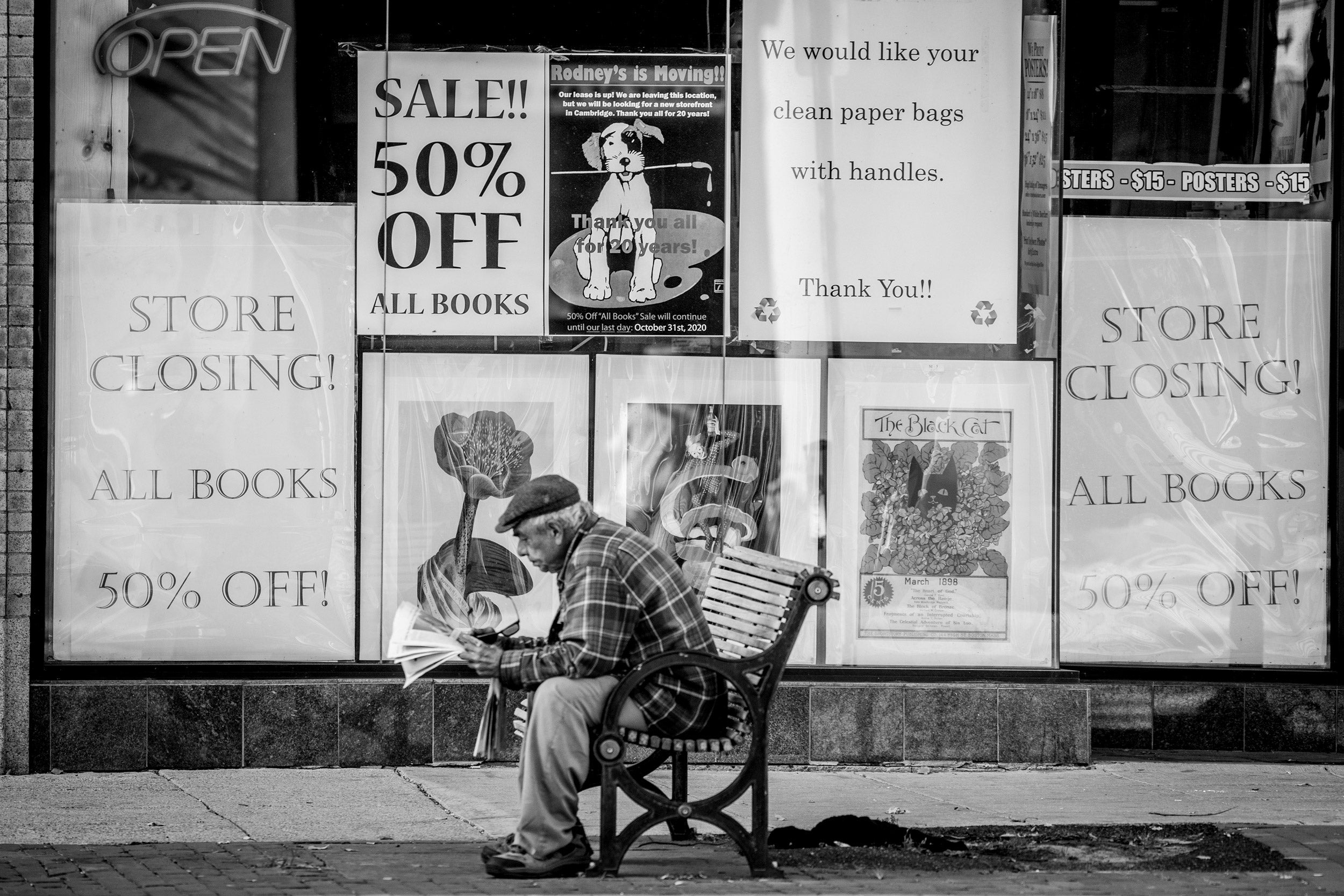 Man sitting on bench in front of store that is closing.